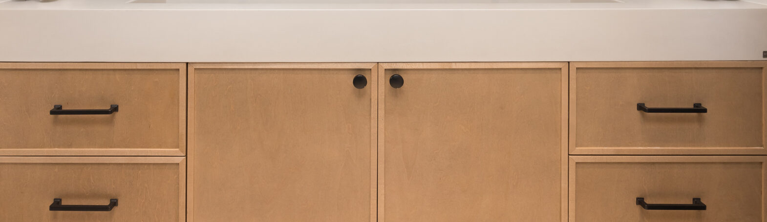 Custom cabinetry in a modern bathroom features light wood finishes with black hardware and a sleek white countertop, all set against a blue subway tile backsplash in Breckenridge, Colorado.