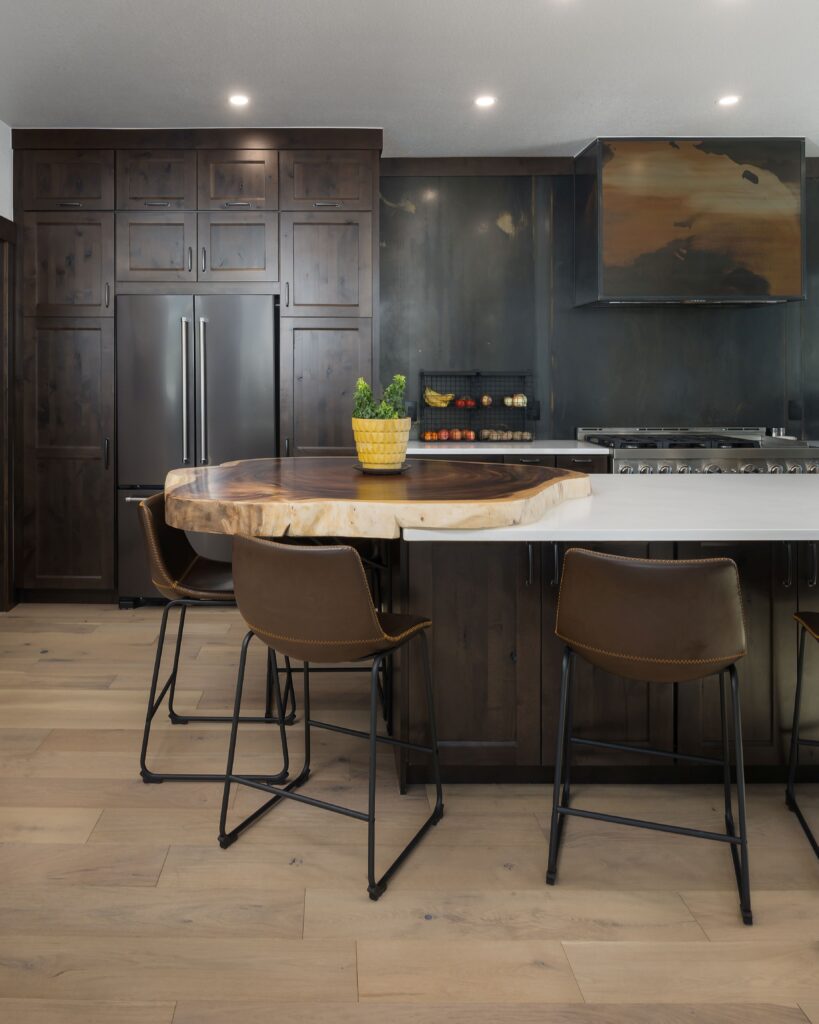 Contemporary kitchen with dark wood cabinetry, built-in refrigerator, and a live-edge wood island countertop paired with leather bar stools. A modern gas range with custom hood and matte backsplash completes the space.